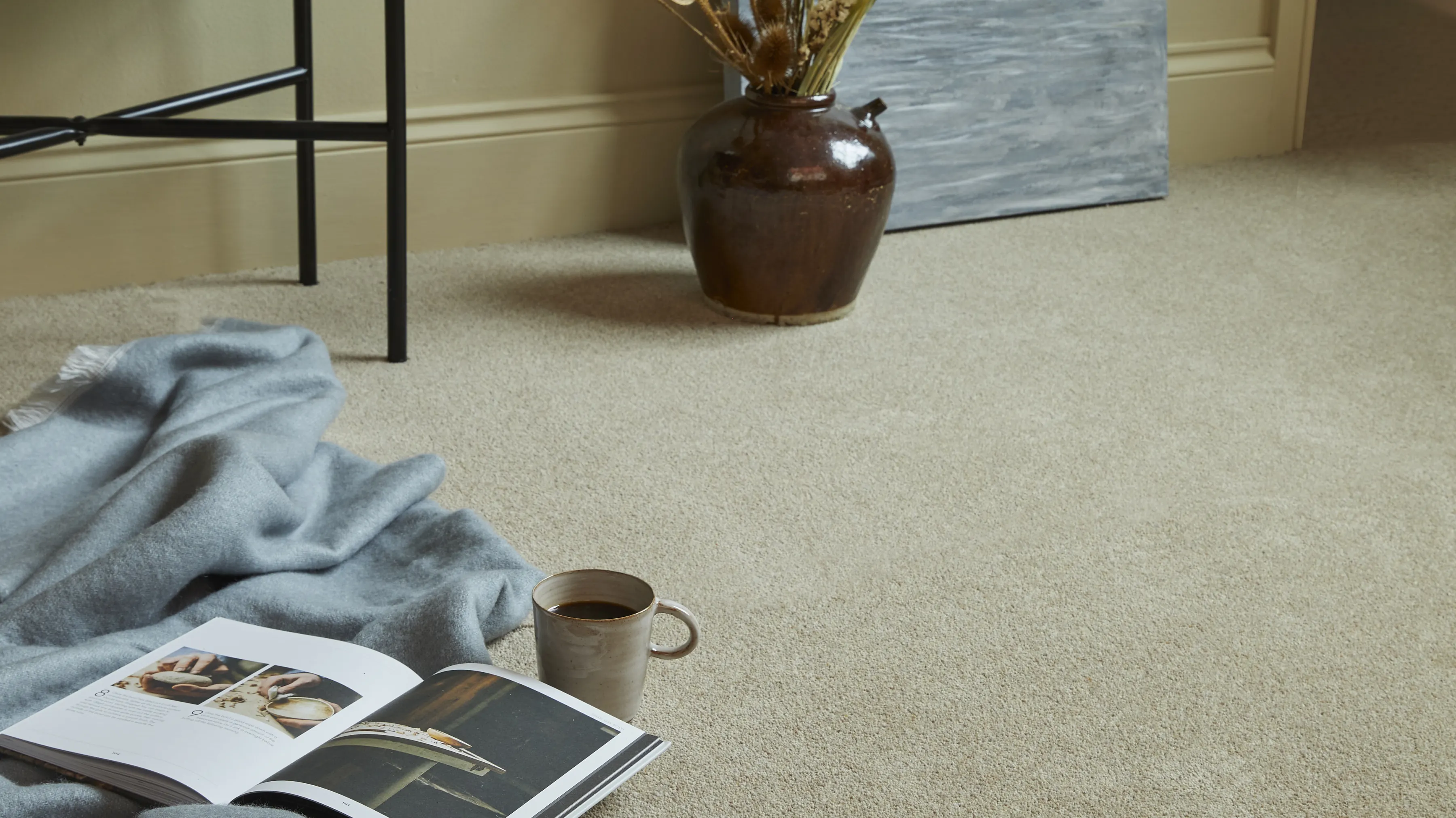 A wool twist carpet fitted neatly into the corner of a room, a throw and a magazine on the floor