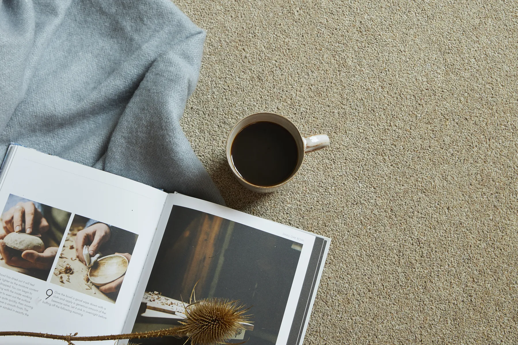 A wool twist carpet seen from above with a throw and a cup of coffee